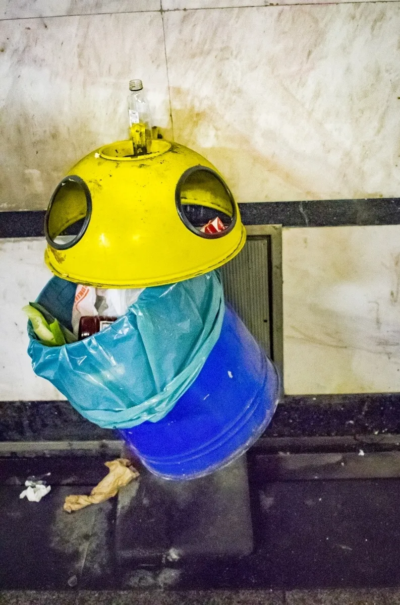 Yellow and blue public trash bin with a bottle balanced on top